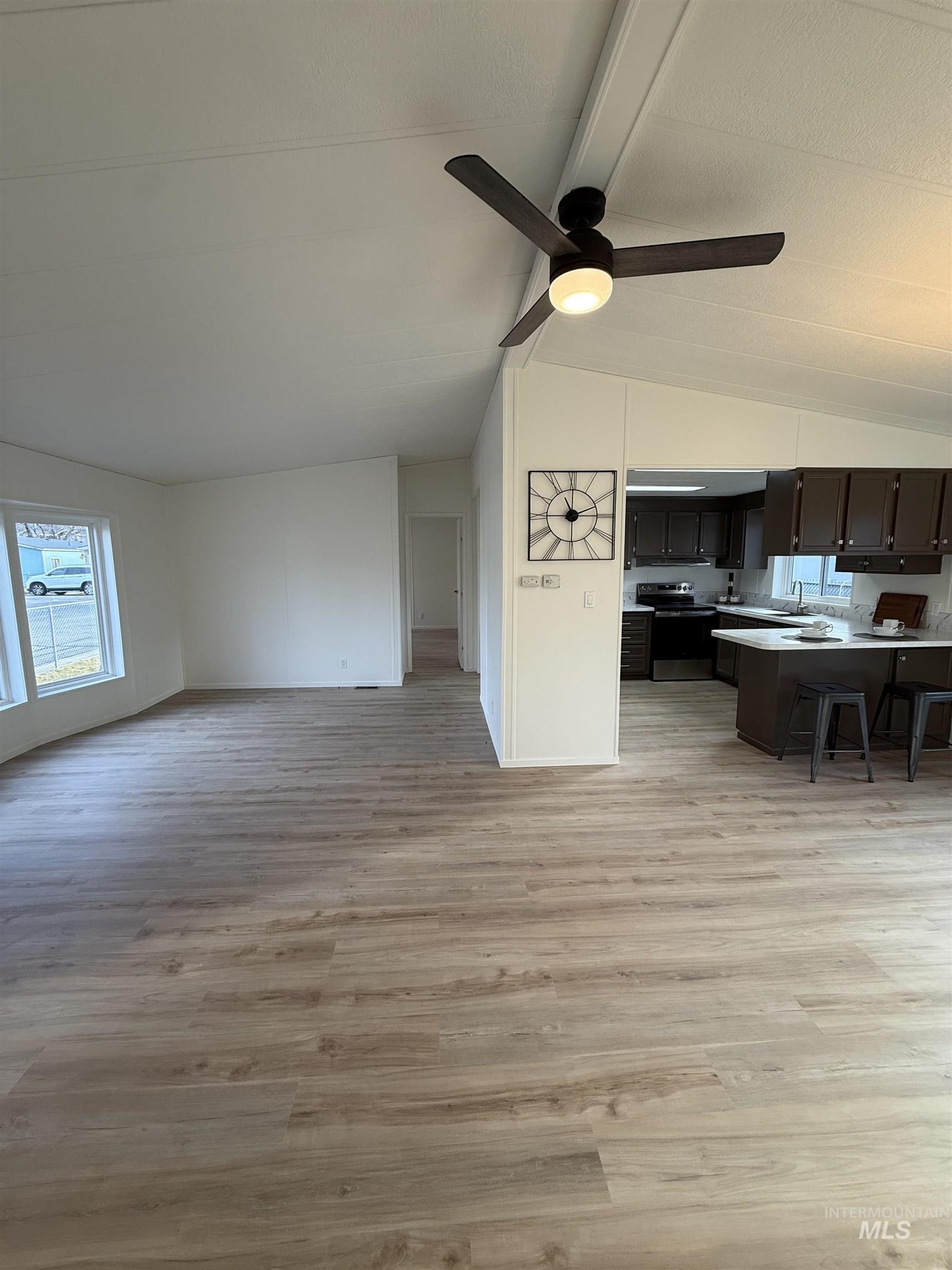 Living area featuring light wood-style flooring, ceiling fan, and lofted ceiling with beams