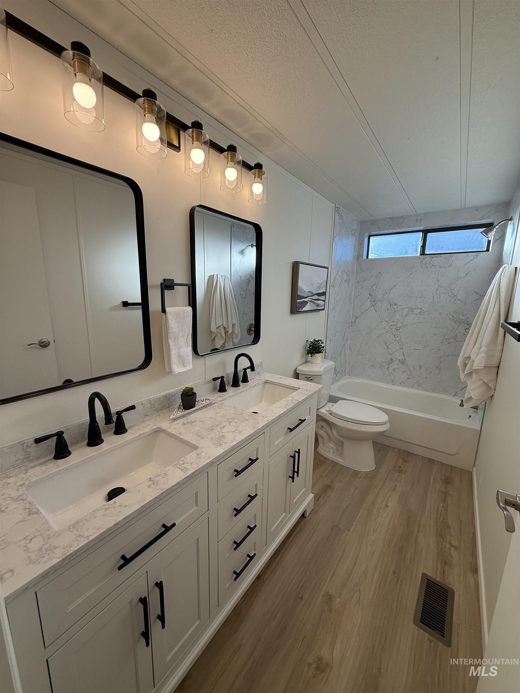 Bathroom with  shower combination, double vanity, light wood-style flooring, and a textured ceiling
