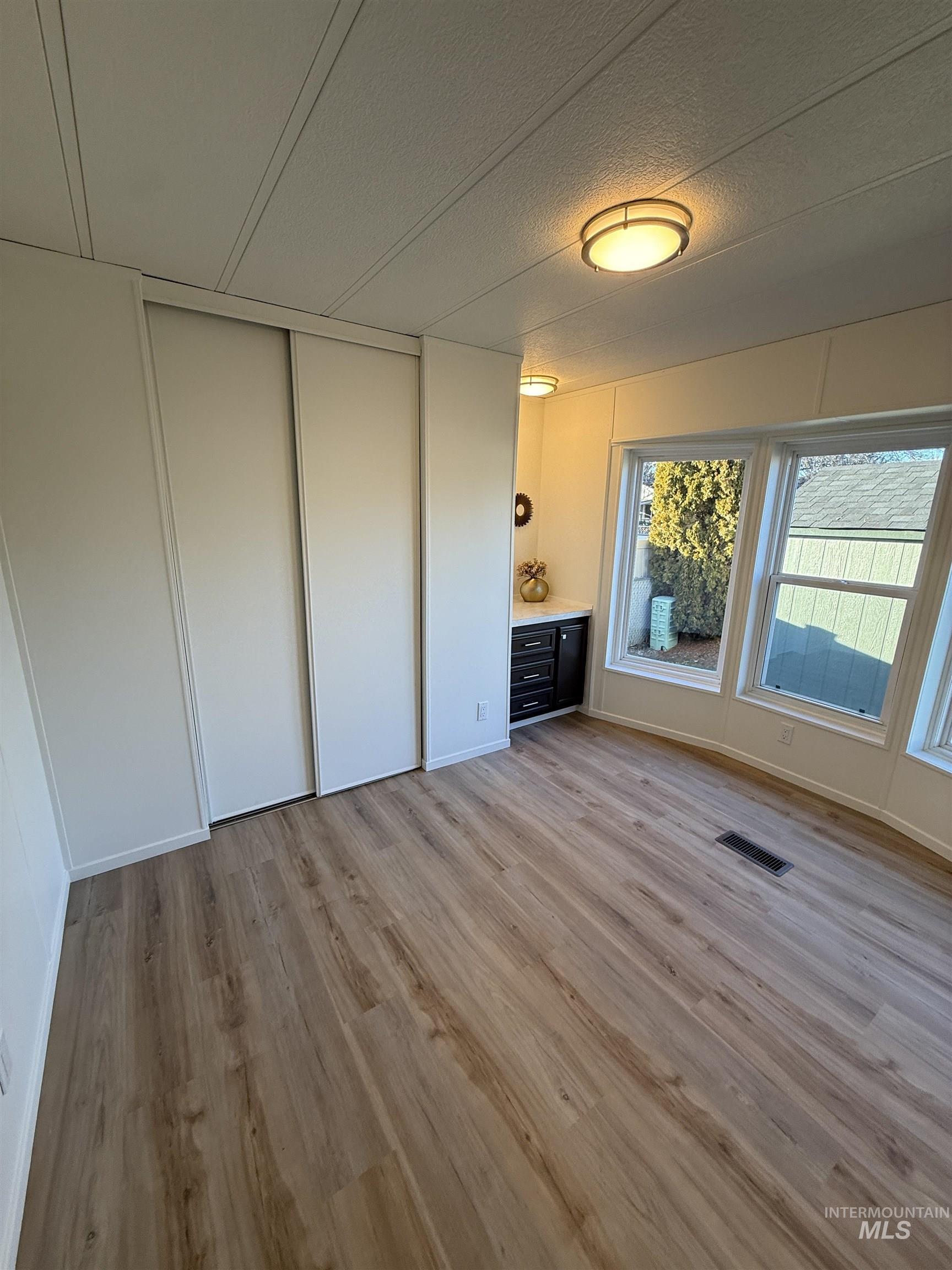 Unfurnished bedroom with a textured ceiling, light wood-style floors, a closet, and a decorative wall