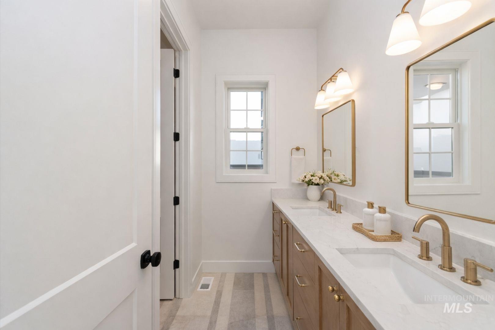 Dual vanity featuring light-toned wood cabinetry, white stone countertops, and gold-finish fixtures
