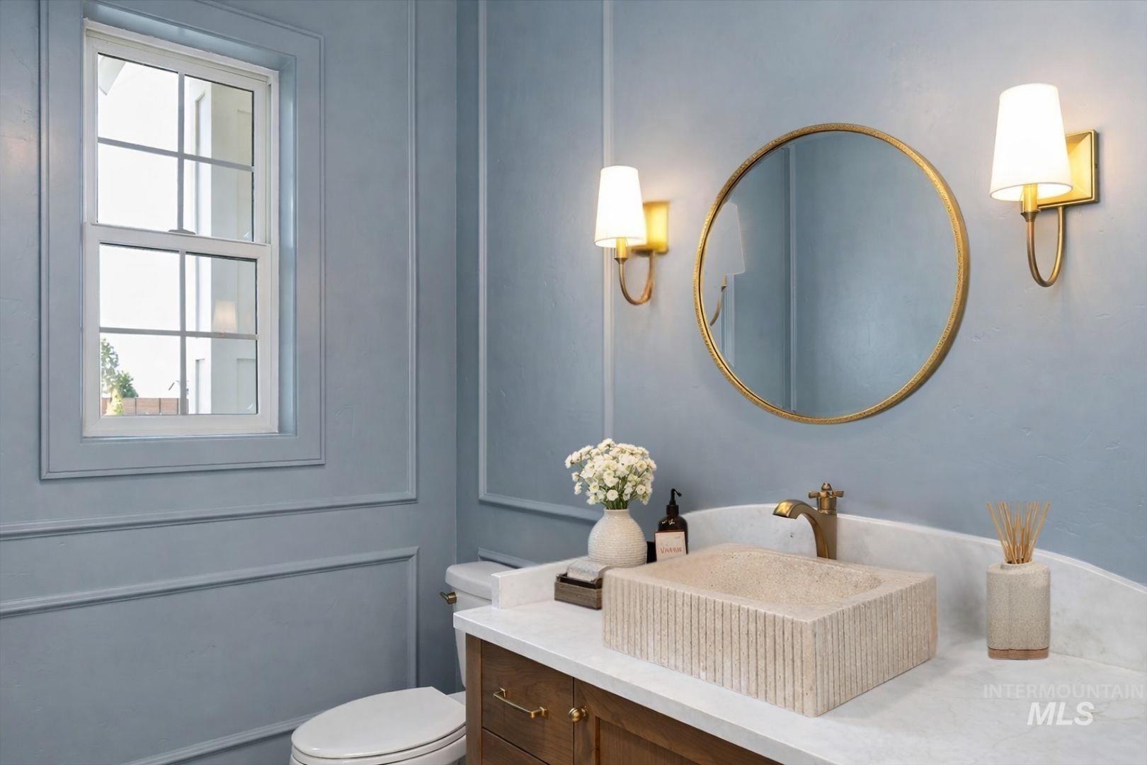 Powder room featuring a rectangular stone vessel sink, brass-finish faucet, and coordinating brass-finish wall sconces