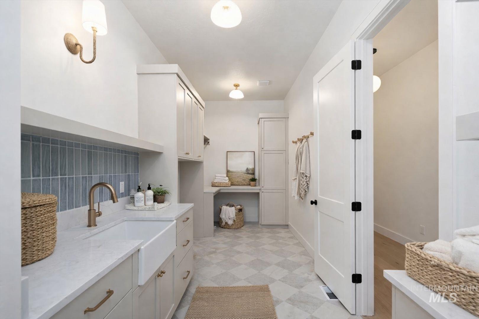 Laundry room featuring a large farmhouse sink, quartz-finish countertop, blue subway tile backsplash, and extensive built-in cabinetry