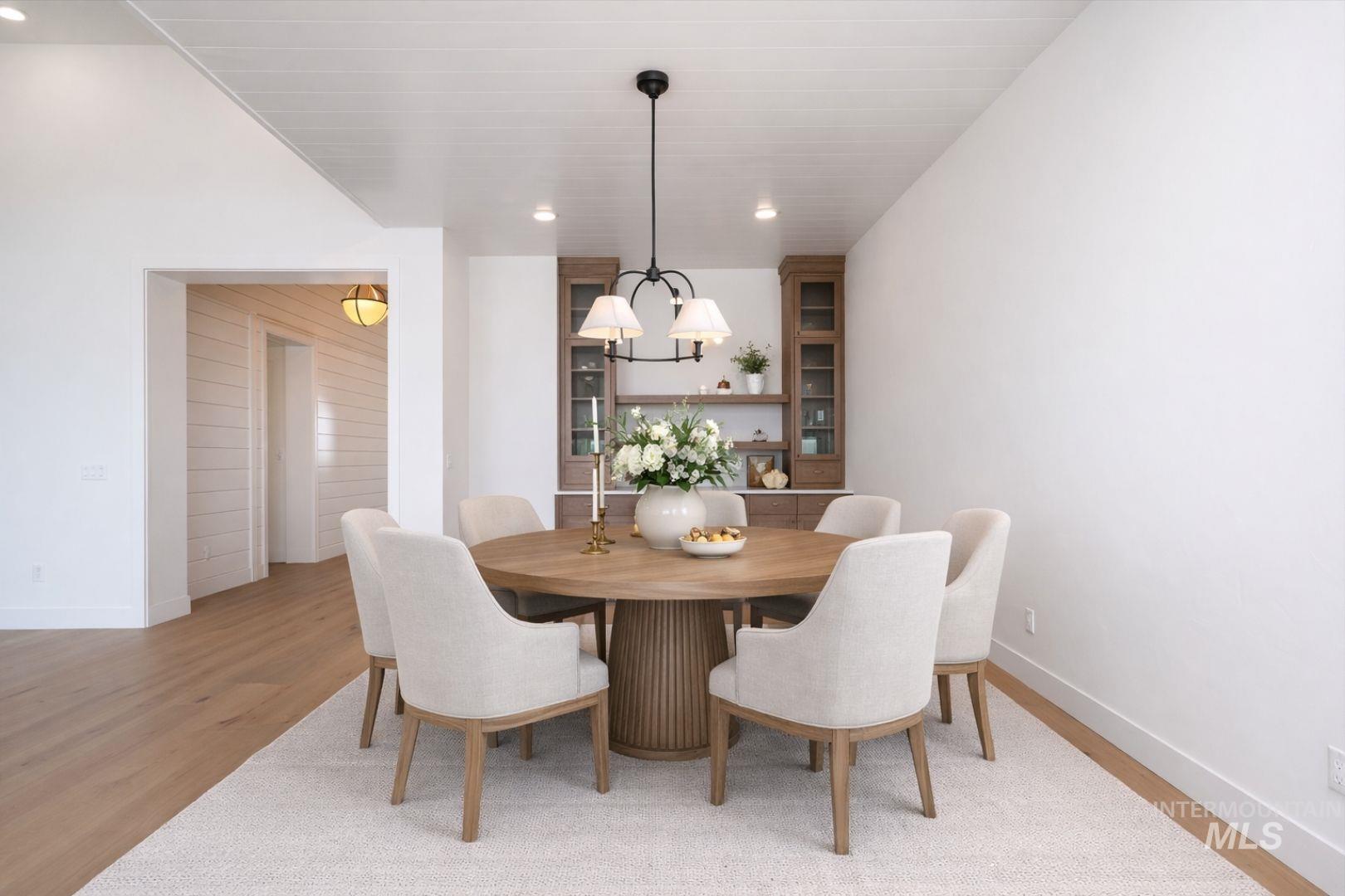 Dining area featuring a contemporary chandelier, built-in cabinetry with glass doors, and light wood-finish flooring