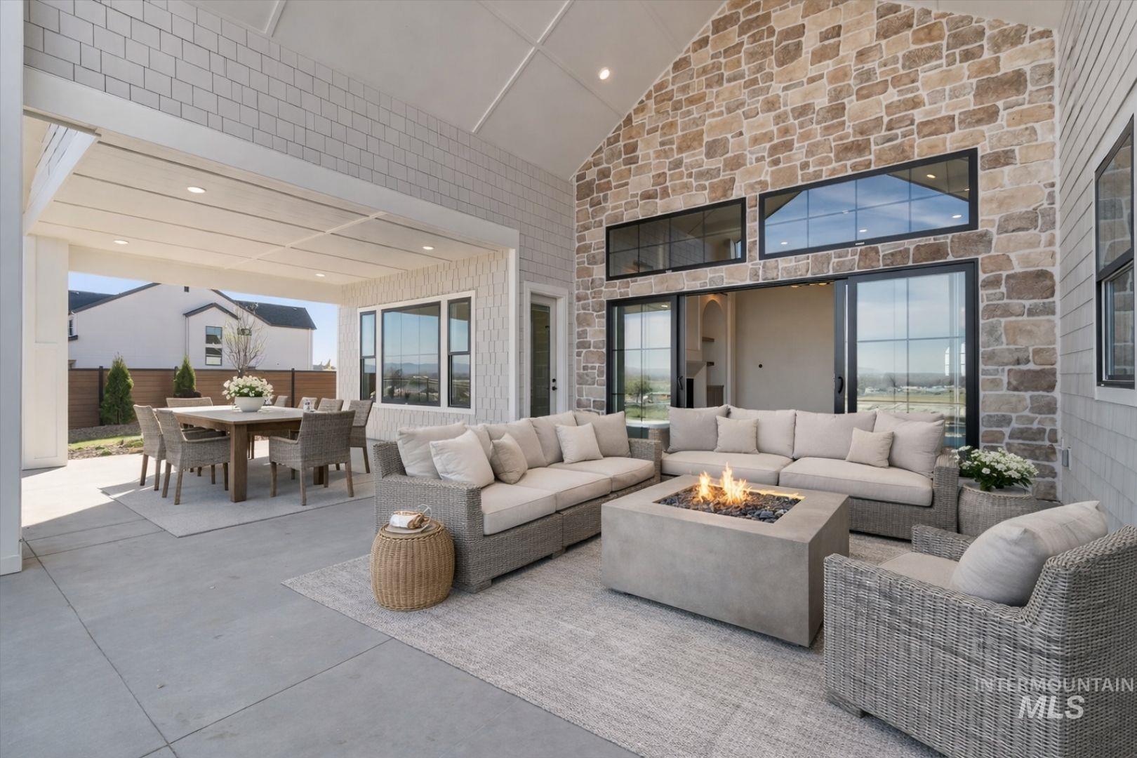 Expansive covered patio featuring a soaring vaulted ceiling, stone accent wall, large sliding glass doors, and recessed lighting