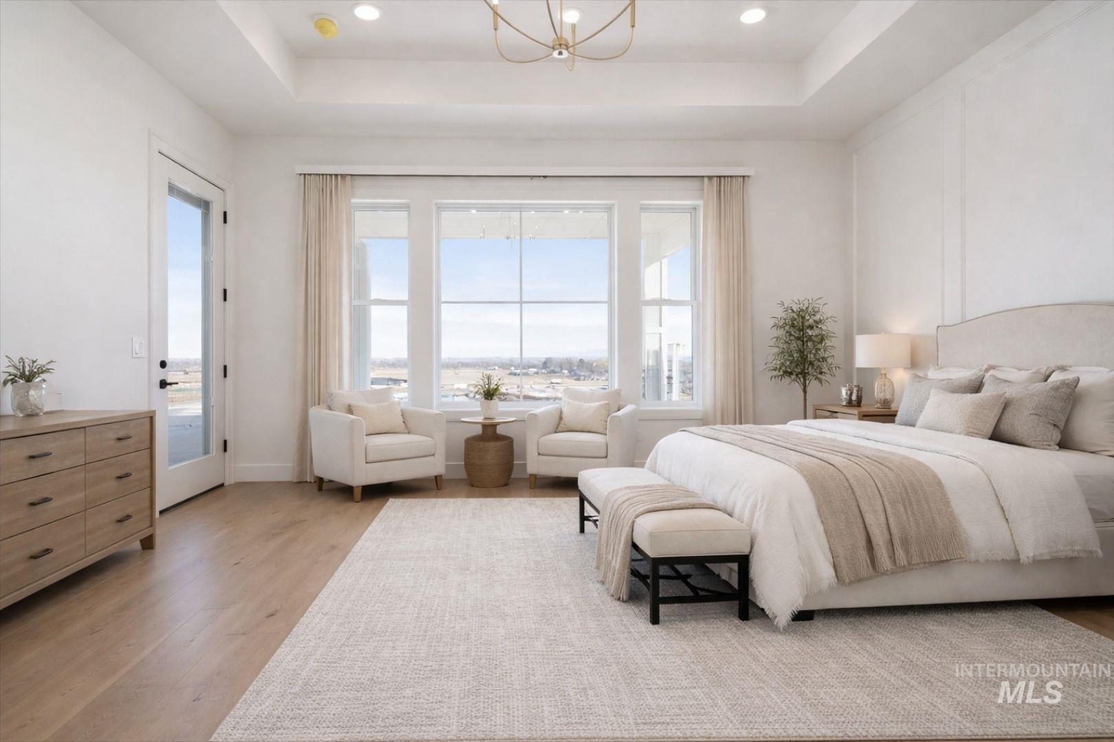 Spacious room featuring light wood-finish flooring, a tray ceiling with recessed lighting, large windows, and a glass-paneled door