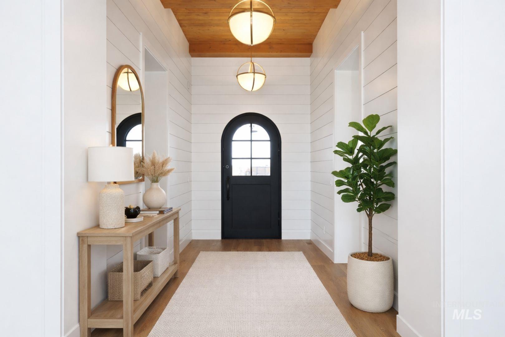 Inviting entry hall featuring a dark arched door, wood-finish flooring, and shiplap wall paneling