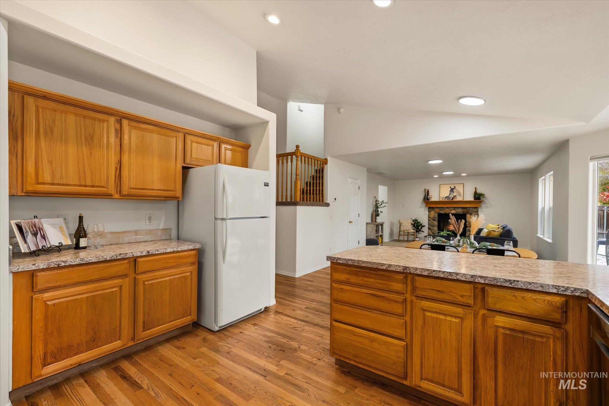 Kitchen featuring brown cabinetry, recessed lighting, freestanding refrigerator, a fireplace, and vaulted ceiling