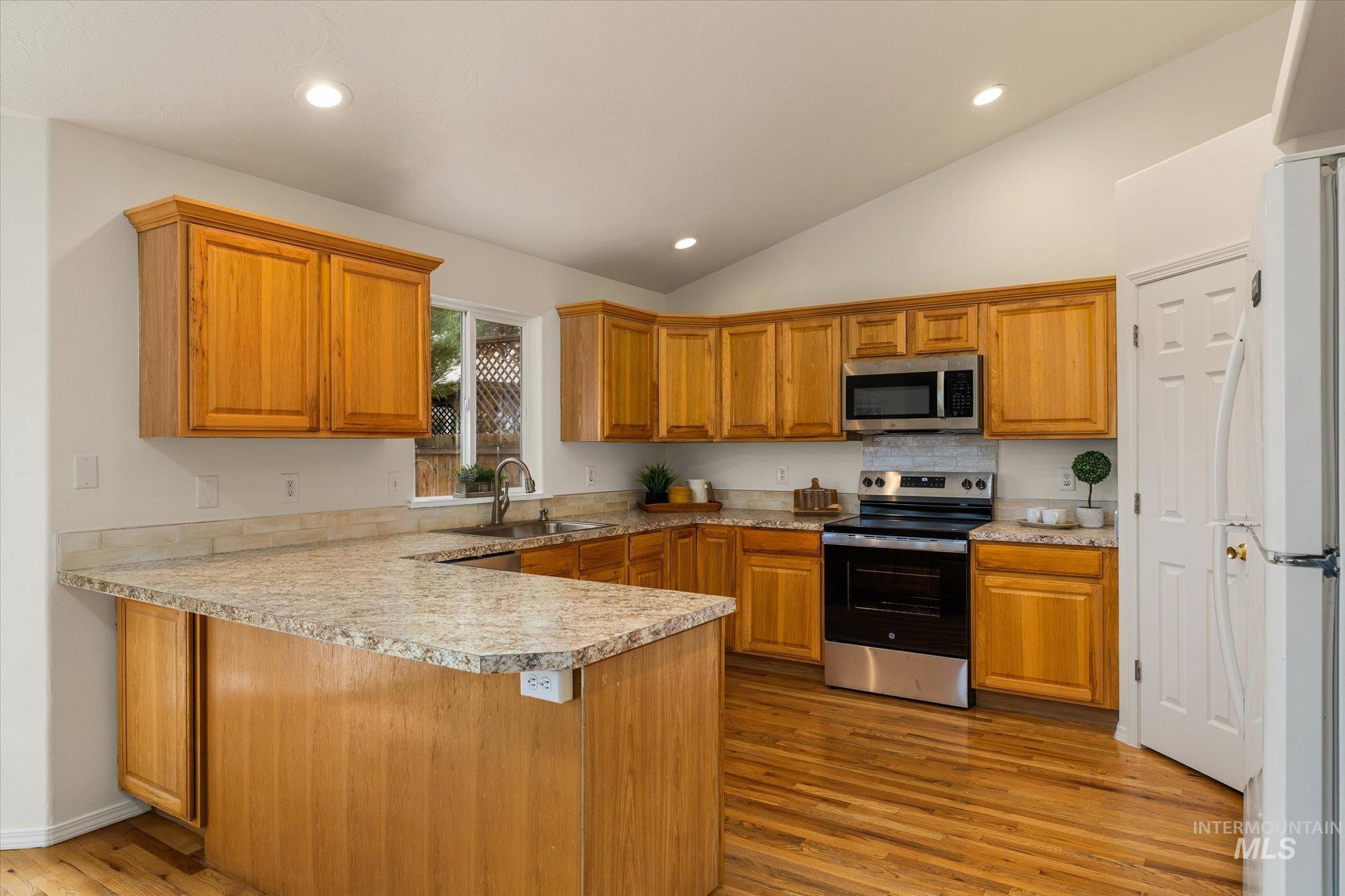 Kitchen with a peninsula, stainless steel appliances, brown cabinets, light wood-type flooring, and recessed lighting