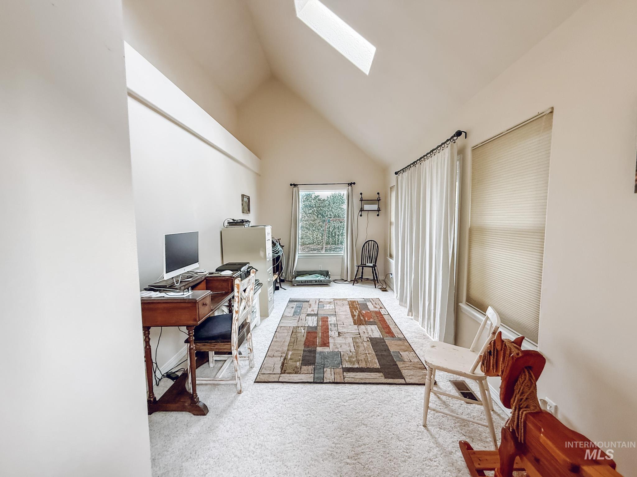 Office area with a skylight, light colored carpet, and high vaulted ceiling