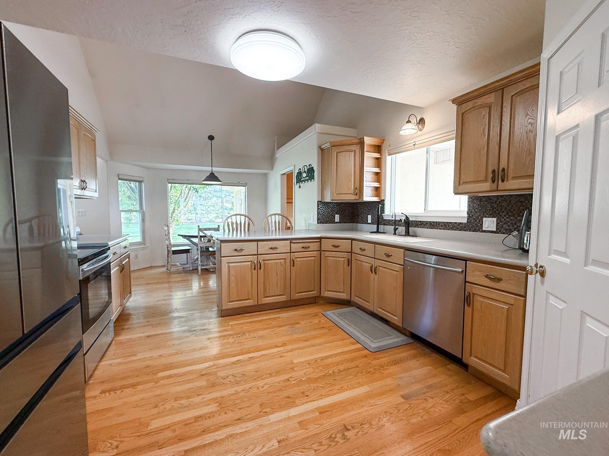 Kitchen featuring stainless steel appliances, light countertops, a peninsula, pendant lighting, and light wood-type flooring