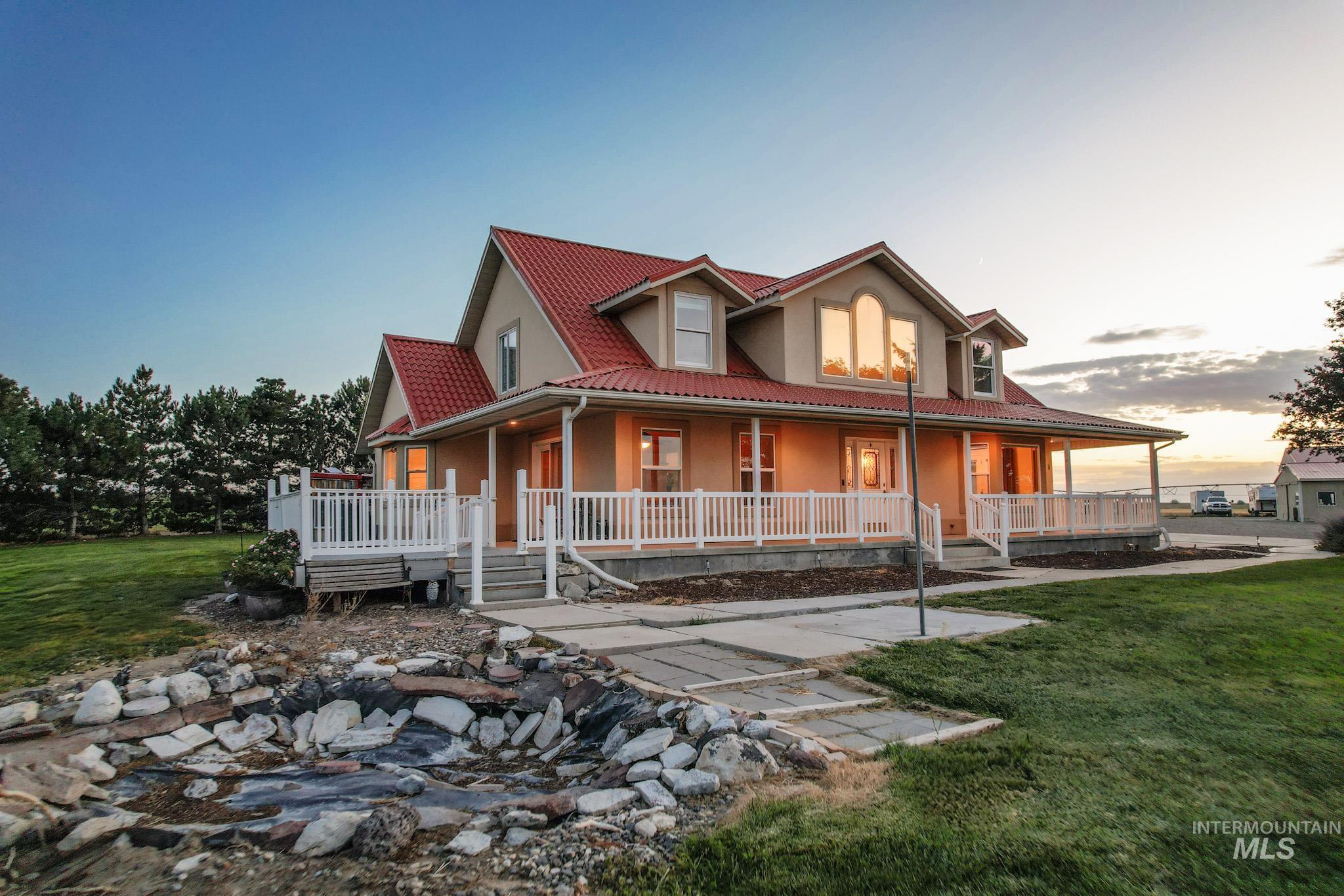 Farmhouse-style home with a lawn, stucco siding, covered porch, and a tiled roof