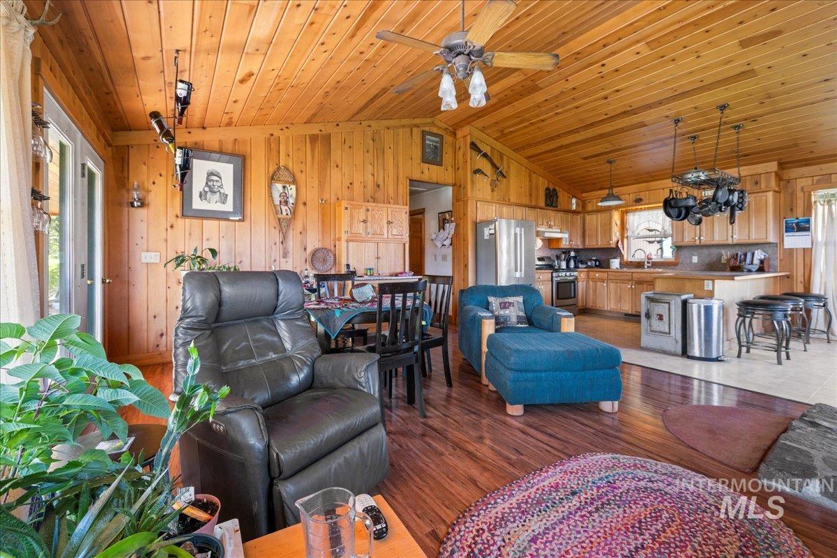 Living area with vaulted ceiling, wood finished floors, wooden walls, wood ceiling, and a ceiling fan