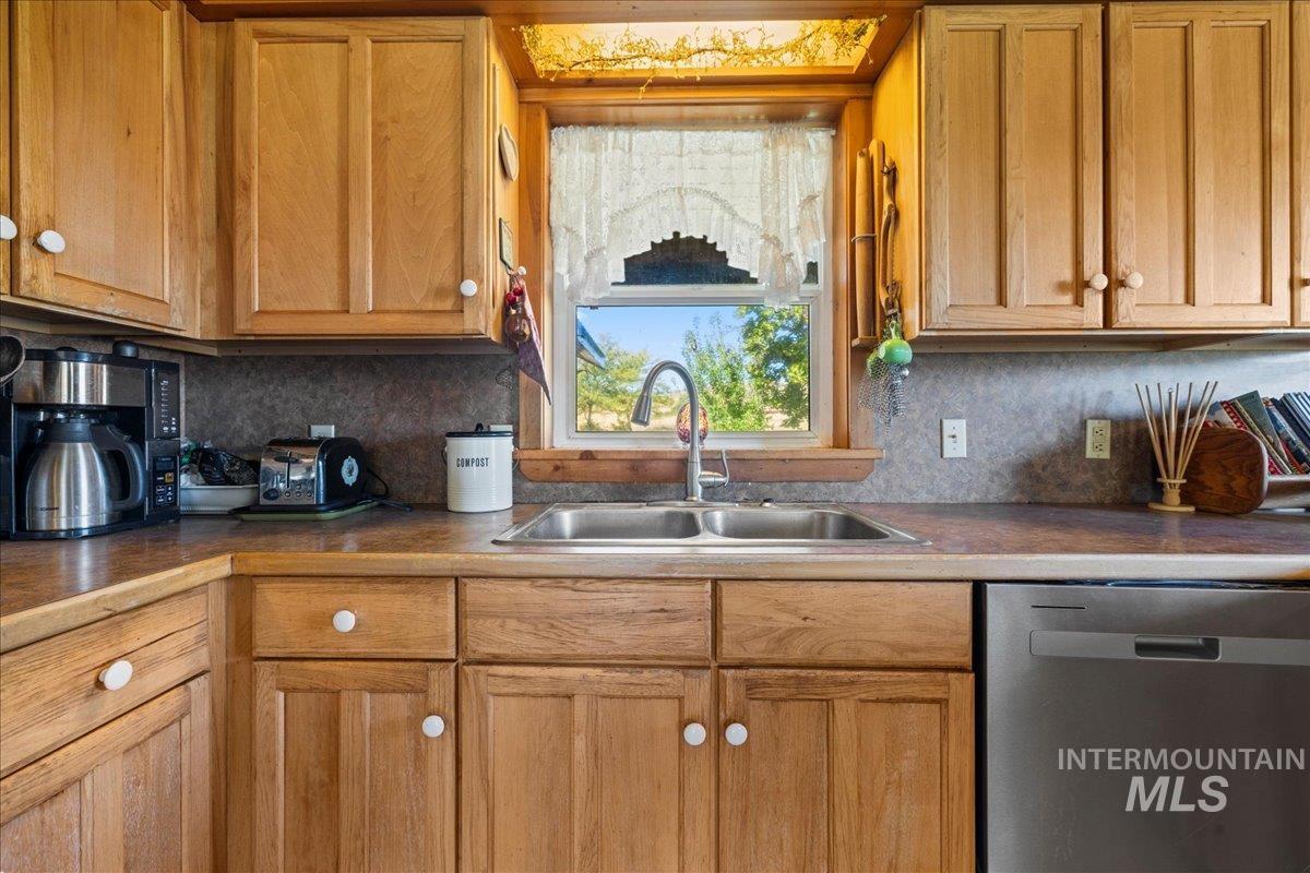 Kitchen with dishwasher, backsplash, brown cabinetry, and dark countertops