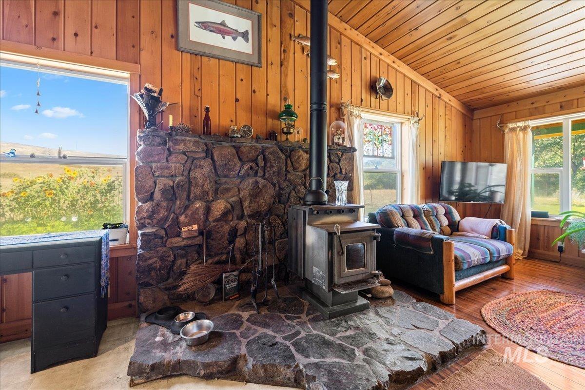 Living room featuring a wood stove, vaulted ceiling, wooden walls, and wood finished floors