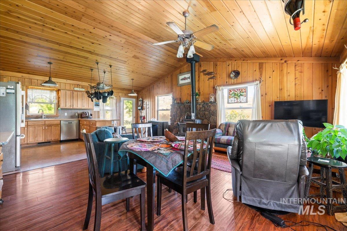 Dining area featuring dark wood-style floors, healthy amount of natural light, lofted ceiling, a wood stove, and wooden walls