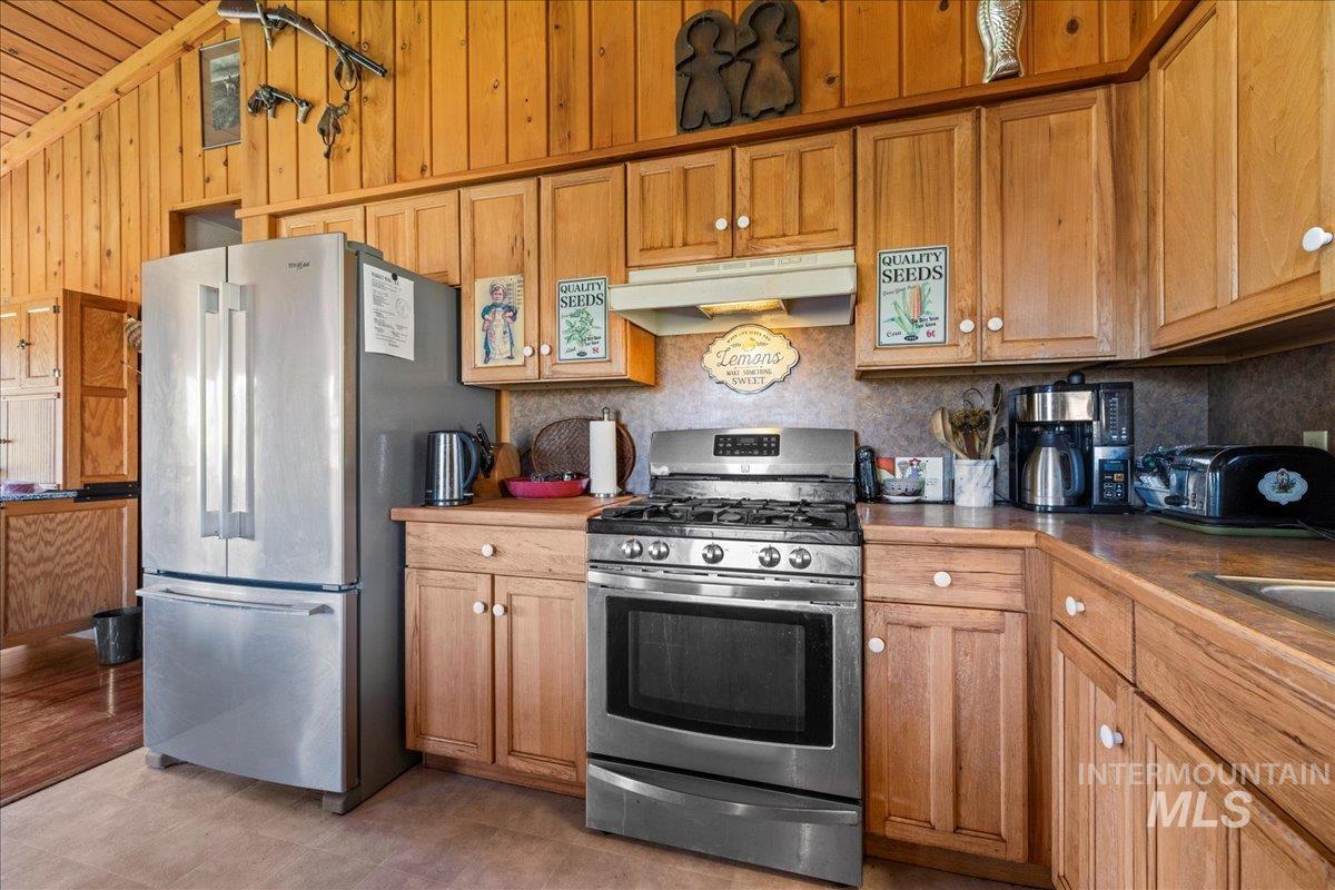 Kitchen featuring appliances with stainless steel finishes, under cabinet range hood, lofted ceiling, decorative backsplash, and brown cabinetry