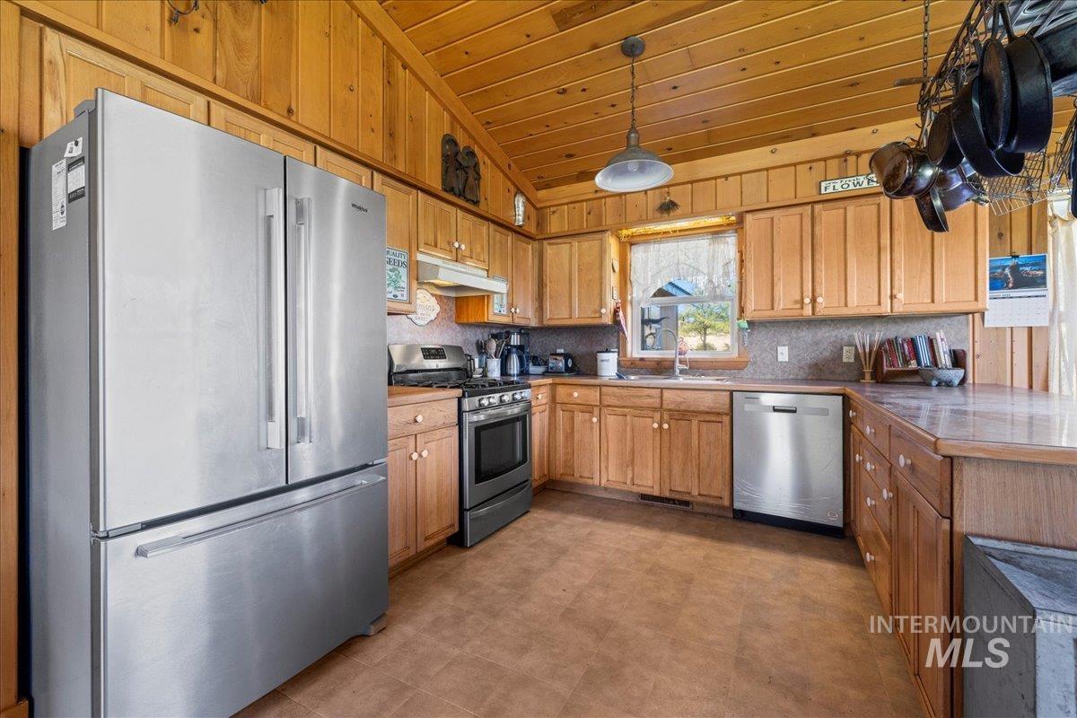 Kitchen featuring appliances with stainless steel finishes, vaulted ceiling, brown cabinetry, a peninsula, and wooden ceiling