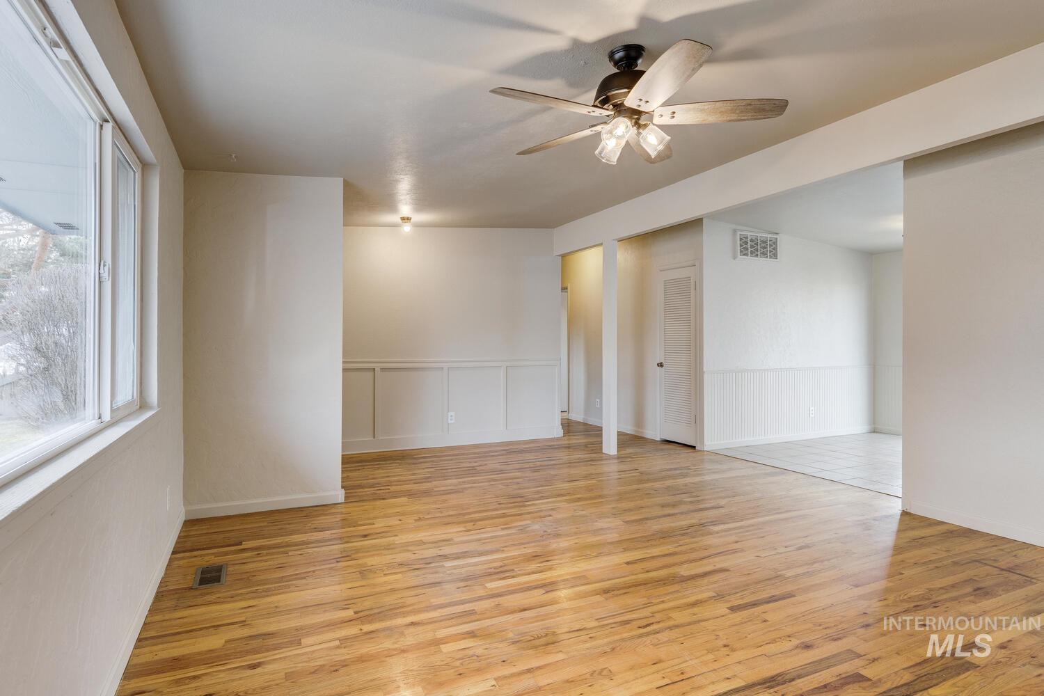 Spare room featuring light wood-style flooring, ceiling fan, and a wainscoted wall