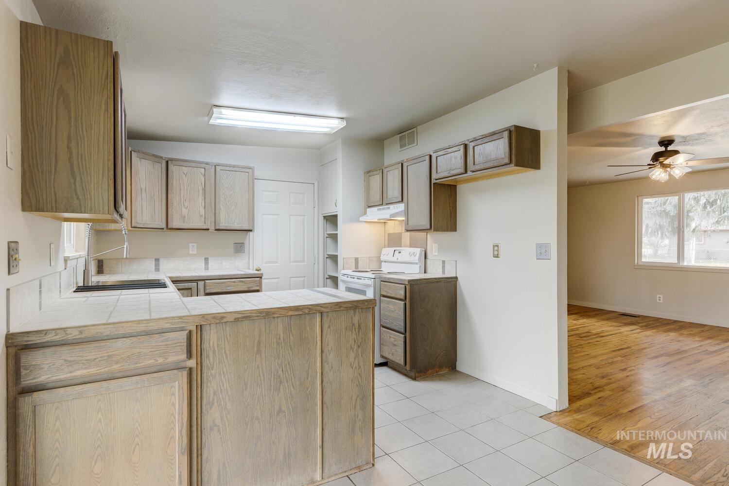 Kitchen with tile countertops, a peninsula, white electric range, light tile patterned floors, and a ceiling fan
