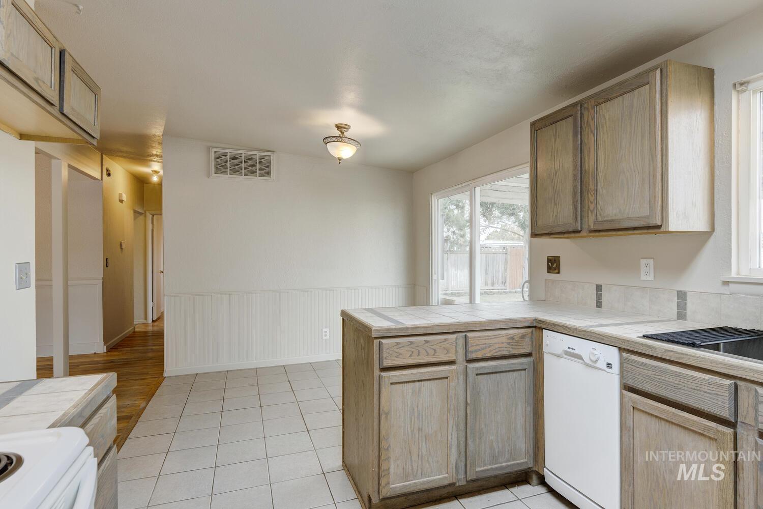 Kitchen featuring tile counters, white appliances, light brown cabinets, a peninsula, and light tile patterned floors