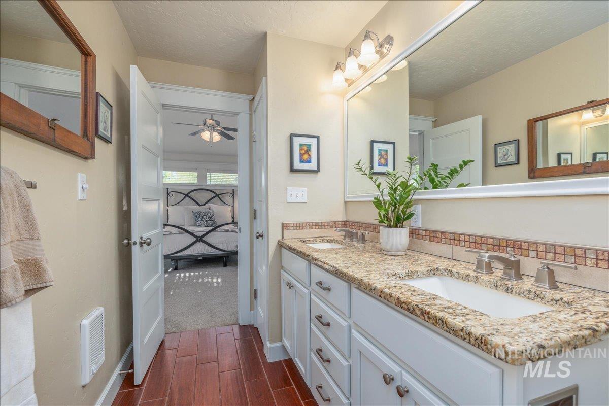 Bathroom with a textured ceiling, double vanity, ensuite bathroom, wood finish floors, and ceiling fan