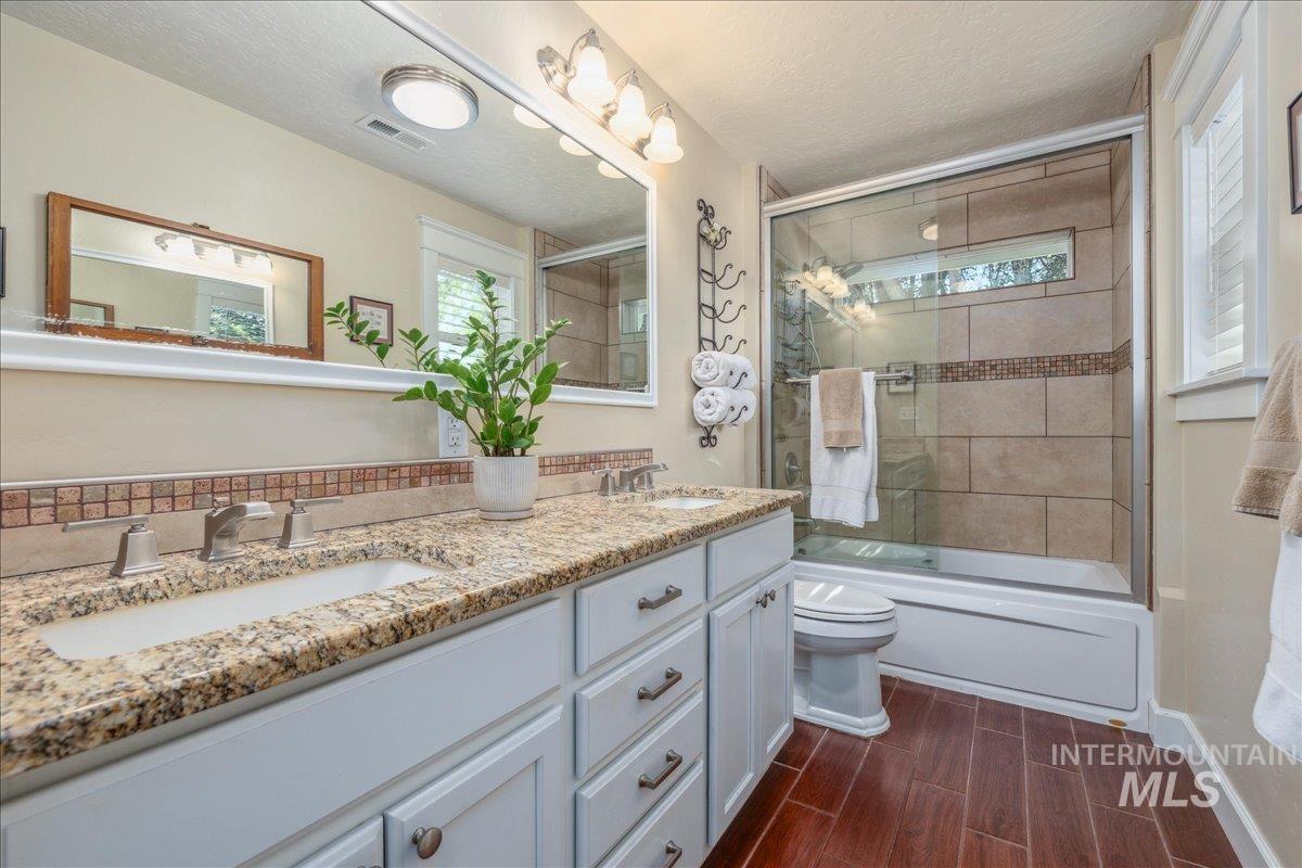 Bathroom featuring bath / shower combo with glass door, a textured ceiling, wood tiled floors, and double vanity
