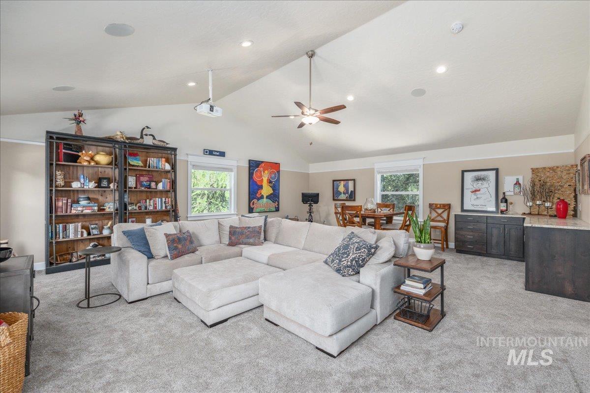 Living area with light colored carpet, plenty of natural light, a ceiling fan, and high vaulted ceiling
