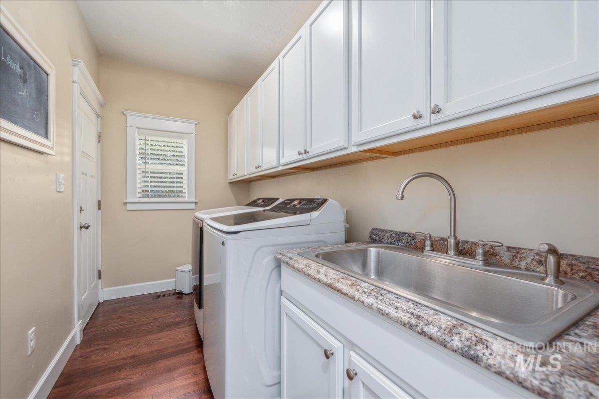 Laundry room with dark wood-style floors, cabinet space, and washer and clothes dryer