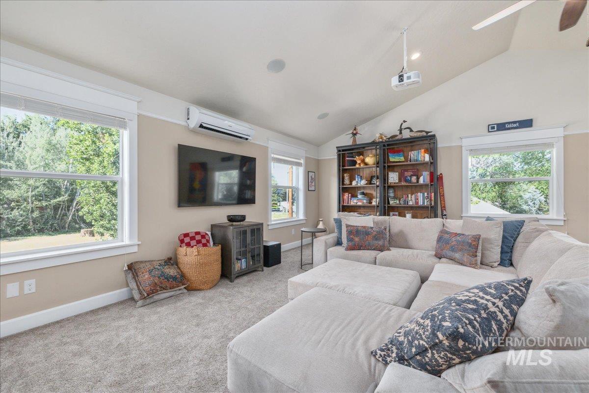 Carpeted living area featuring lofted ceiling, a wall mounted air conditioner, and a ceiling fan