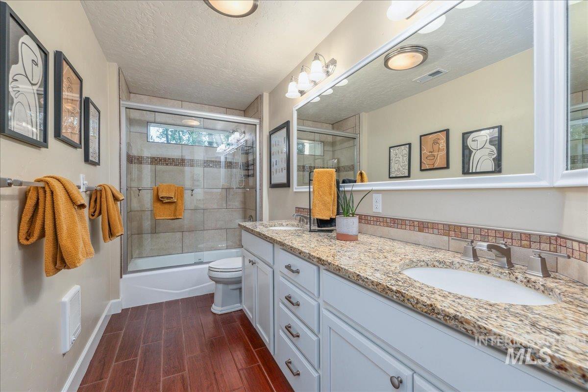 Bathroom featuring combined bath / shower with glass door, double vanity, wood finish floors, and a textured ceiling