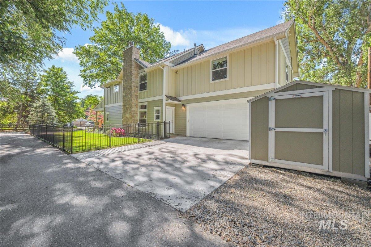 View of front of home featuring concrete driveway, a chimney, a garage, board and batten siding, and a shed