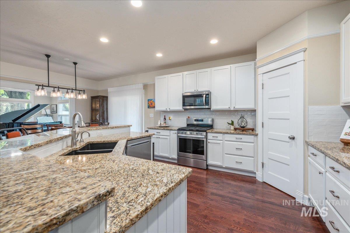 Kitchen featuring decorative light fixtures, appliances with stainless steel finishes, white cabinetry, recessed lighting, and light stone countertops