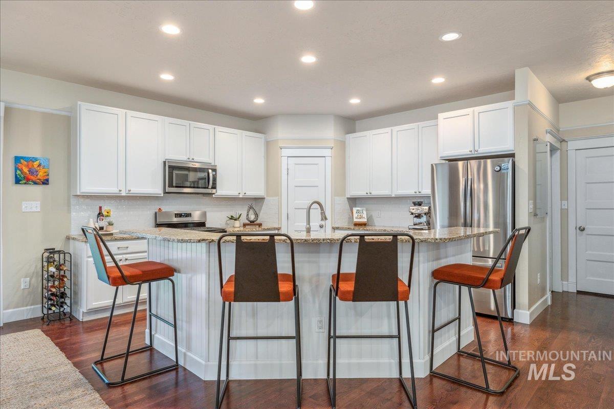 Kitchen featuring a kitchen bar, light stone countertops, a center island with sink, recessed lighting, and appliances with stainless steel finishes
