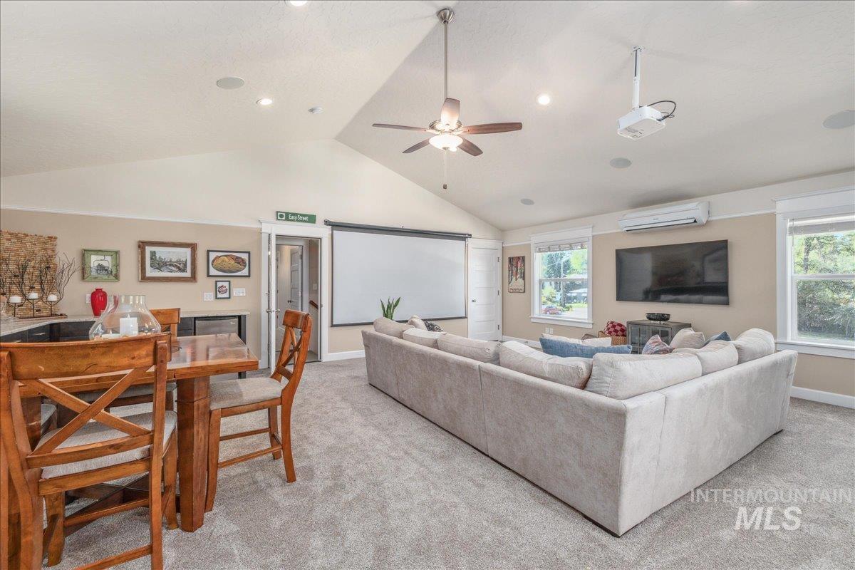 Living area featuring light carpet, high vaulted ceiling, a wall mounted AC, and ceiling fan