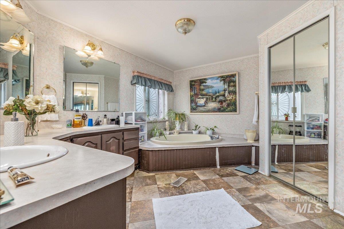 Bathroom with wallpapered walls, two vanities, a garden tub, stone finish flooring, and crown molding