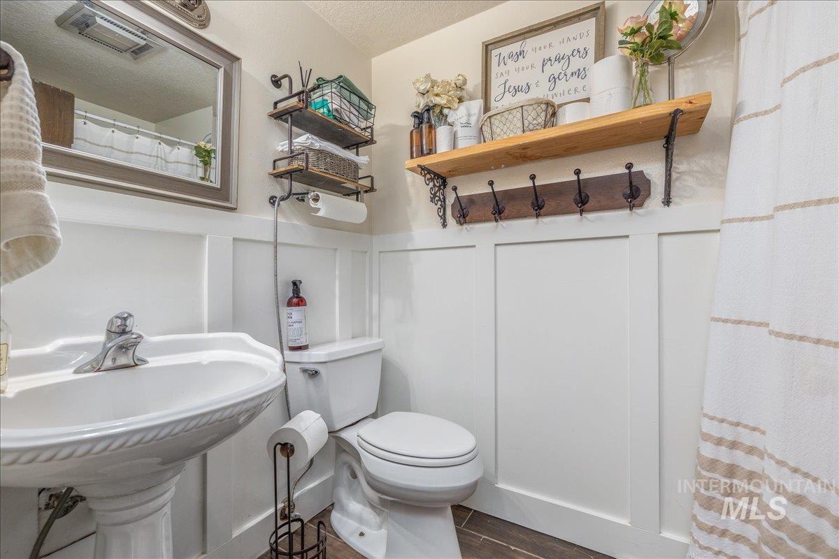 Bathroom with a shower with shower curtain, wood tiled floors, a decorative wall, a wainscoted wall, and a textured ceiling