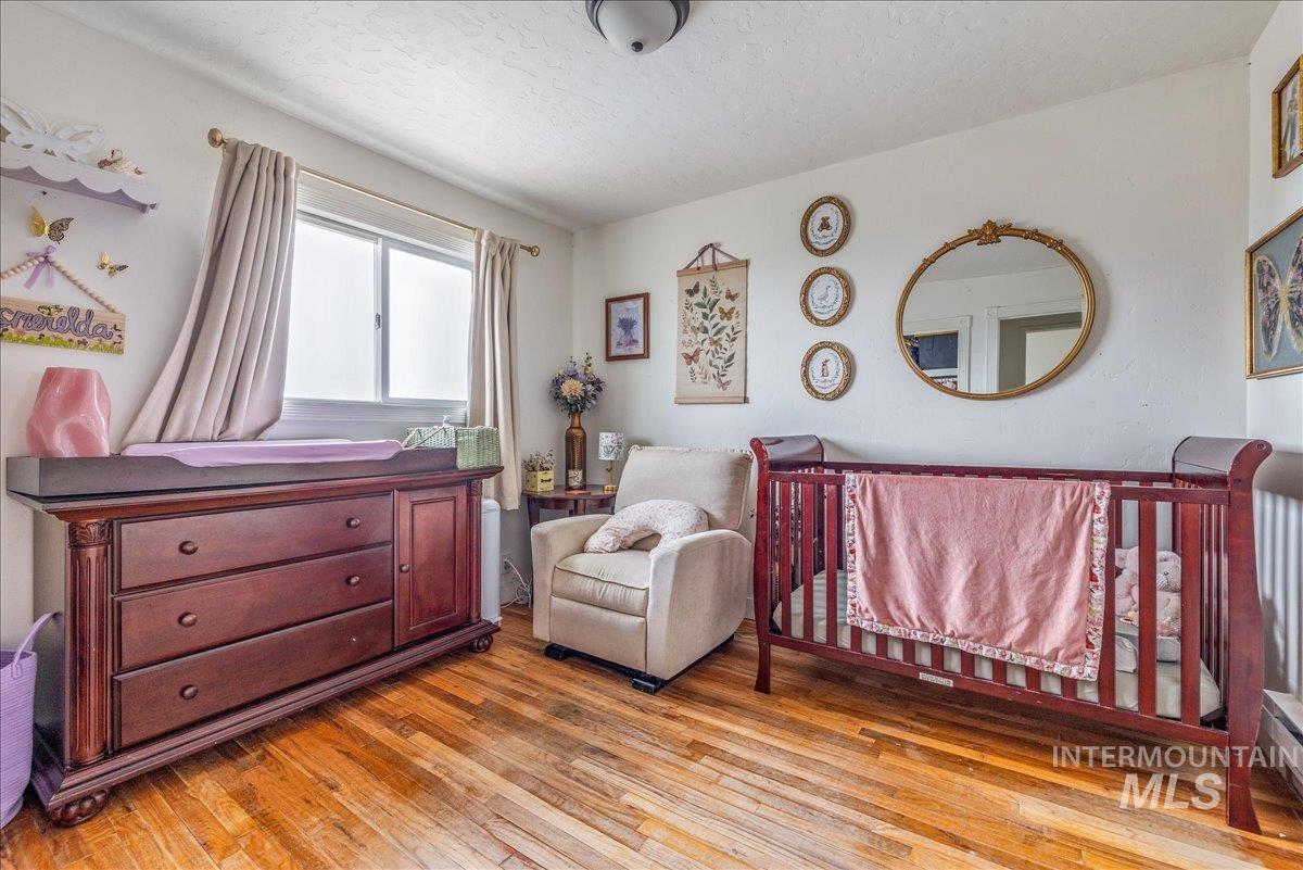 Bedroom with a nursery area, light wood-style flooring, and a textured ceiling