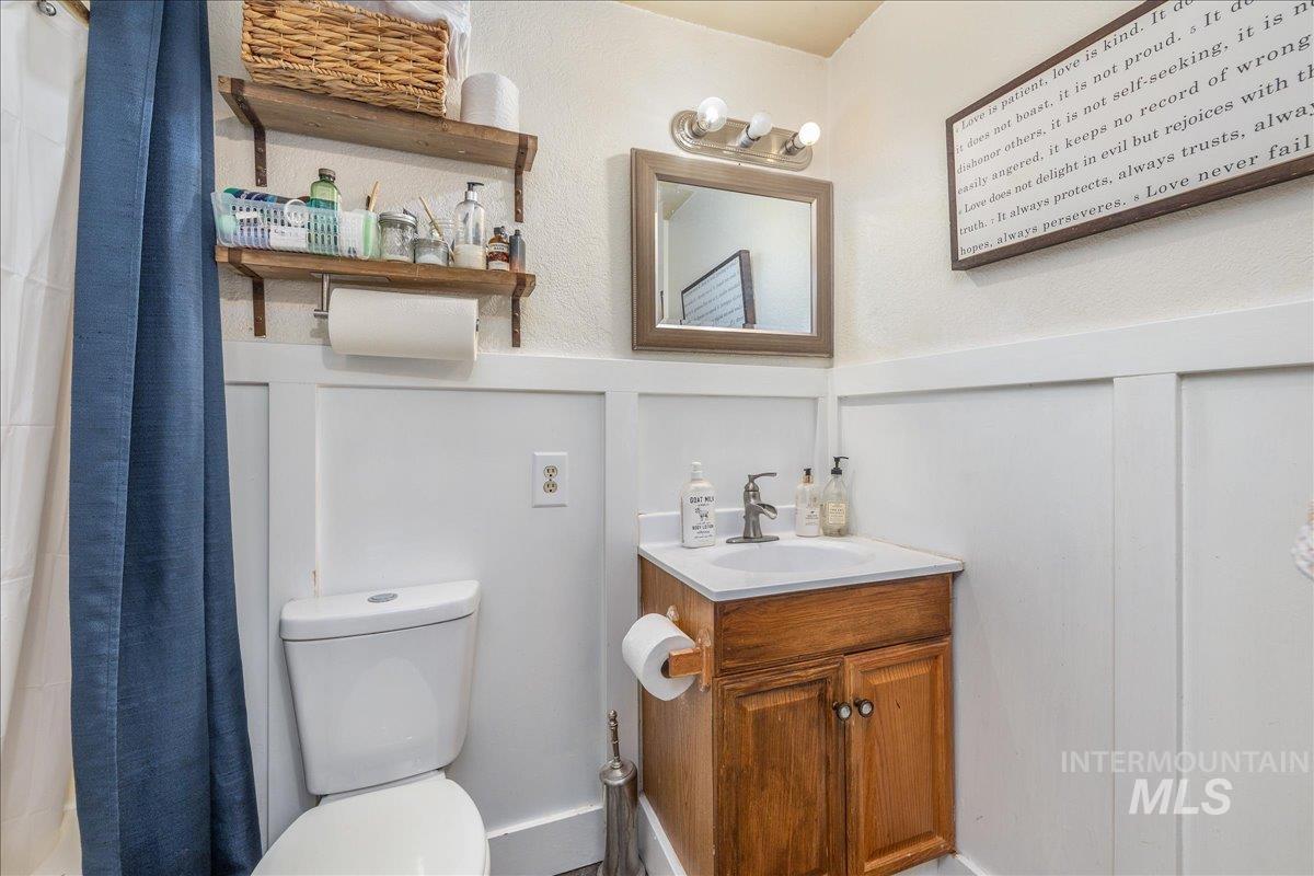 Full bath featuring vanity, curtained shower, wainscoting, and a textured wall