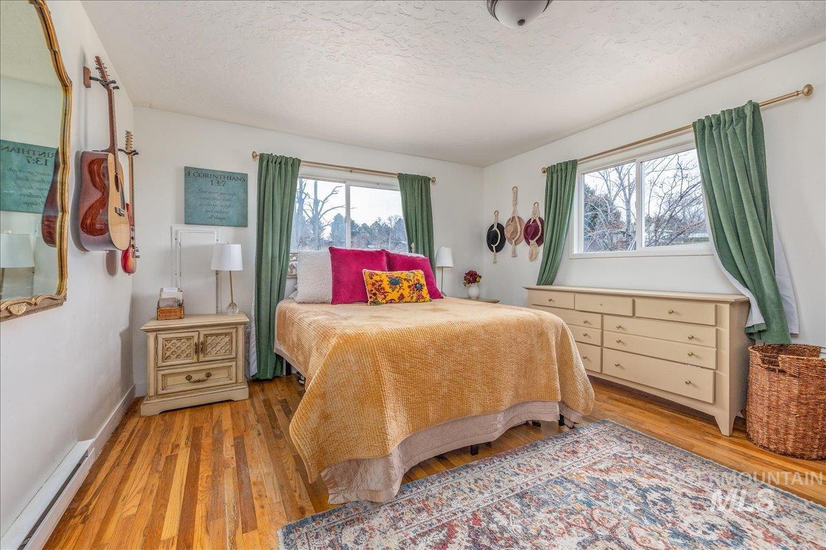Bedroom with baseboard heating, light wood finished floors, and a textured ceiling