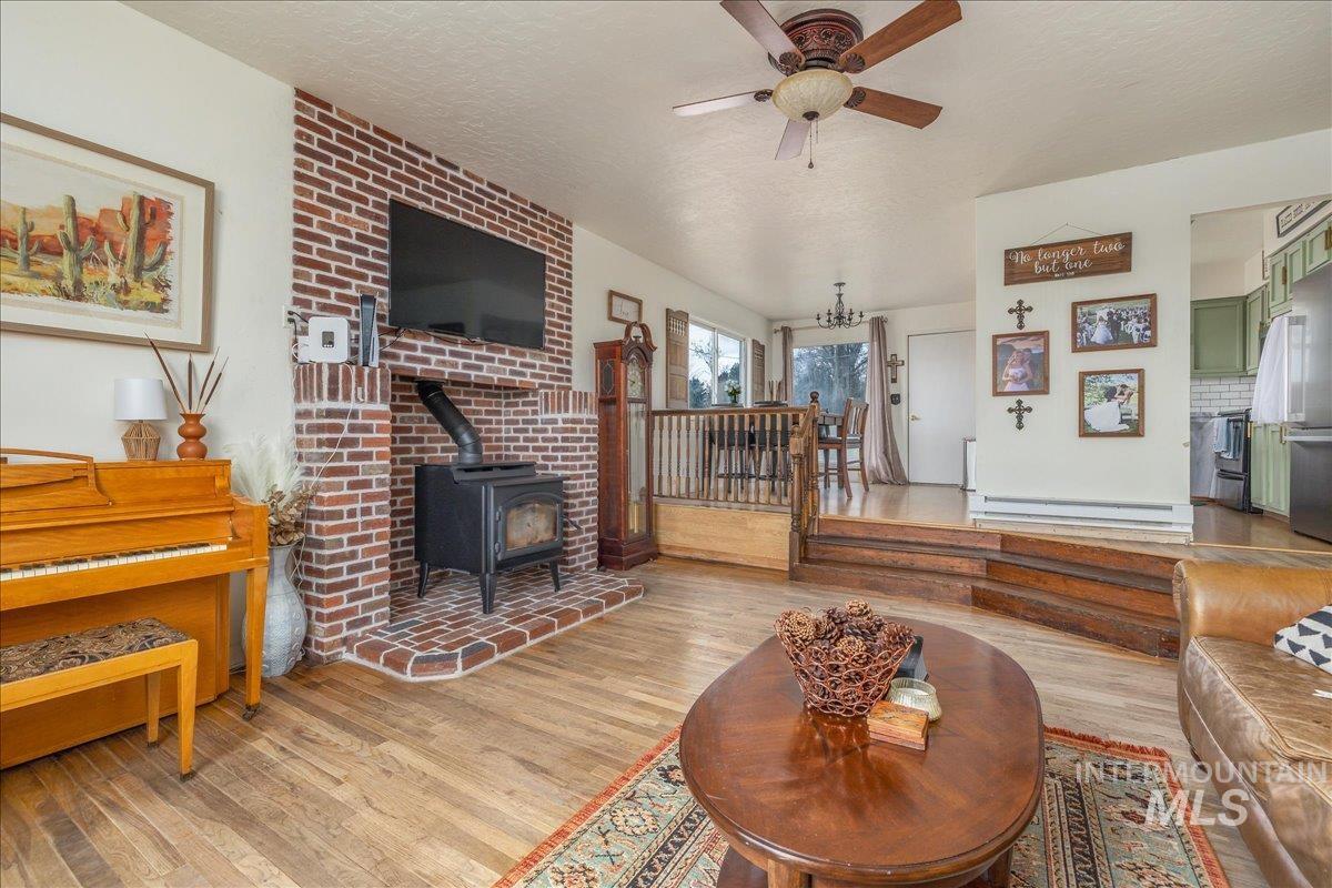 Living area featuring a wood stove, light wood-style flooring, ceiling fan, a textured ceiling, and a baseboard heating unit