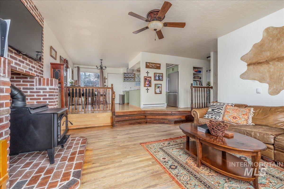 Living room with light wood-style flooring, a wood stove, ceiling fan, a textured ceiling, and a baseboard radiator