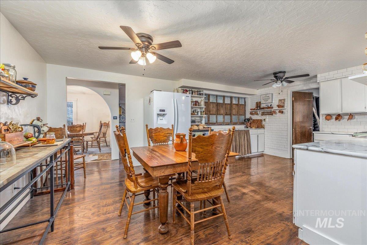 Dining area featuring a ceiling fan, dark wood-style flooring, a textured ceiling, and arched walkways