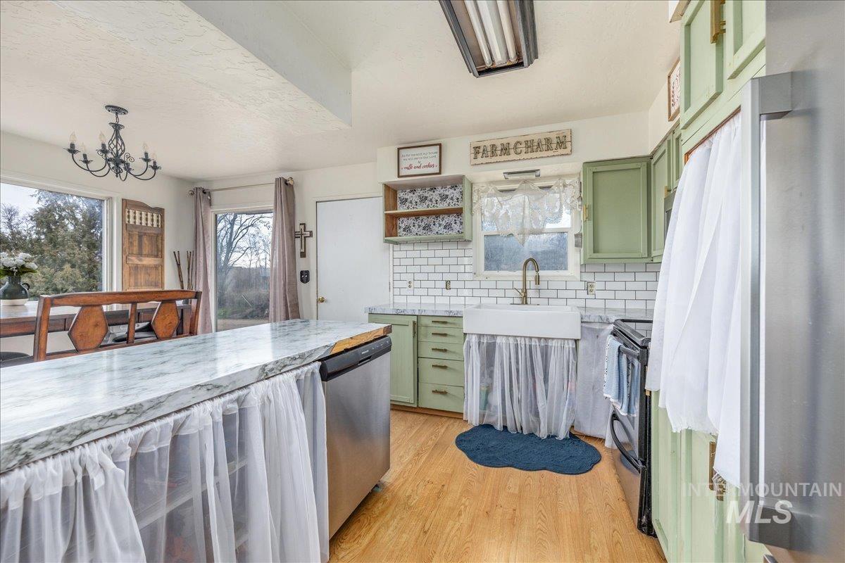 Kitchen with green cabinets, decorative backsplash, open shelves, stainless steel dishwasher, and light wood-style floors