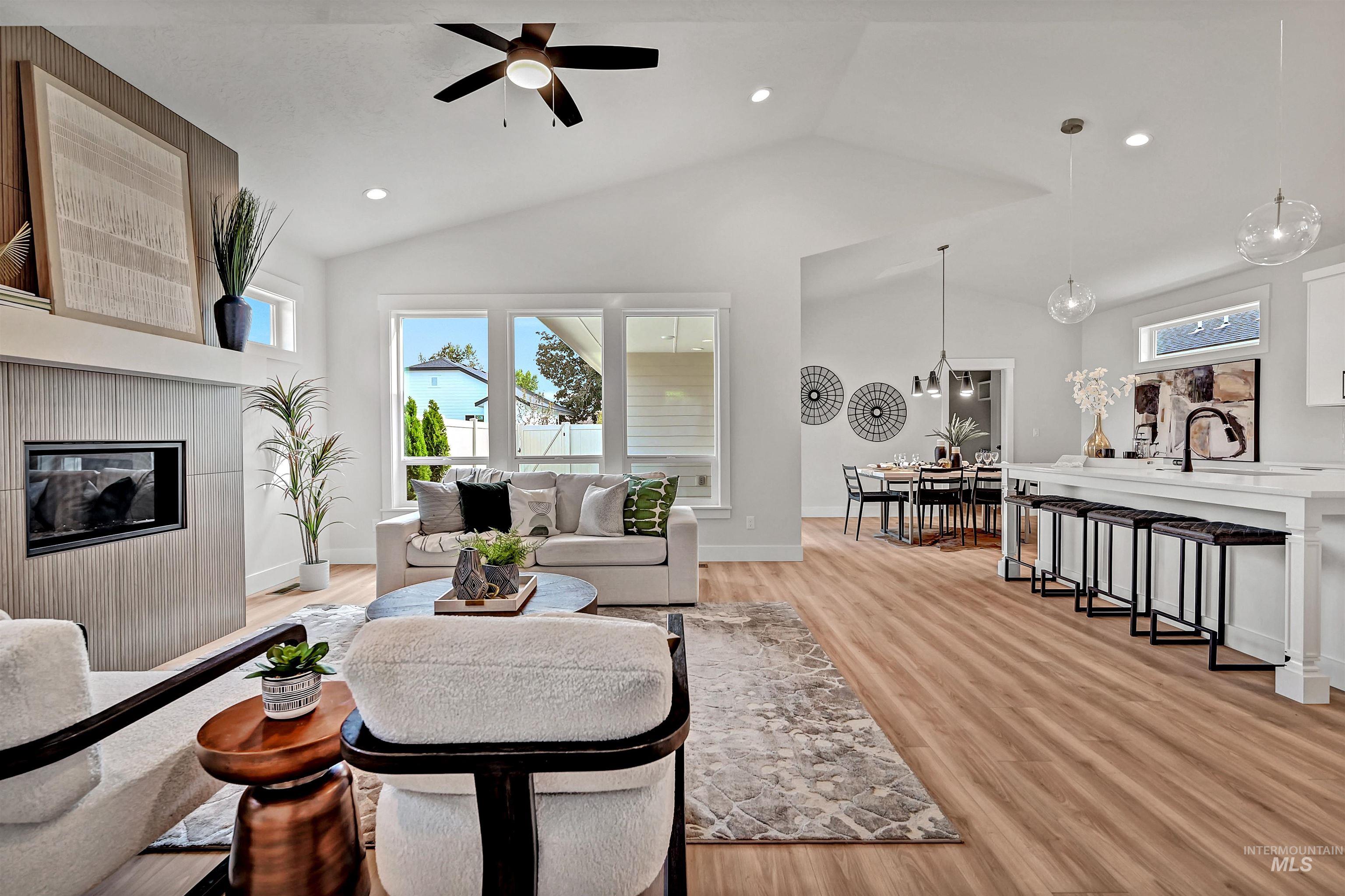 Living room with a tiled fireplace, light wood-style floors, recessed lighting, ceiling fan, and lofted ceiling