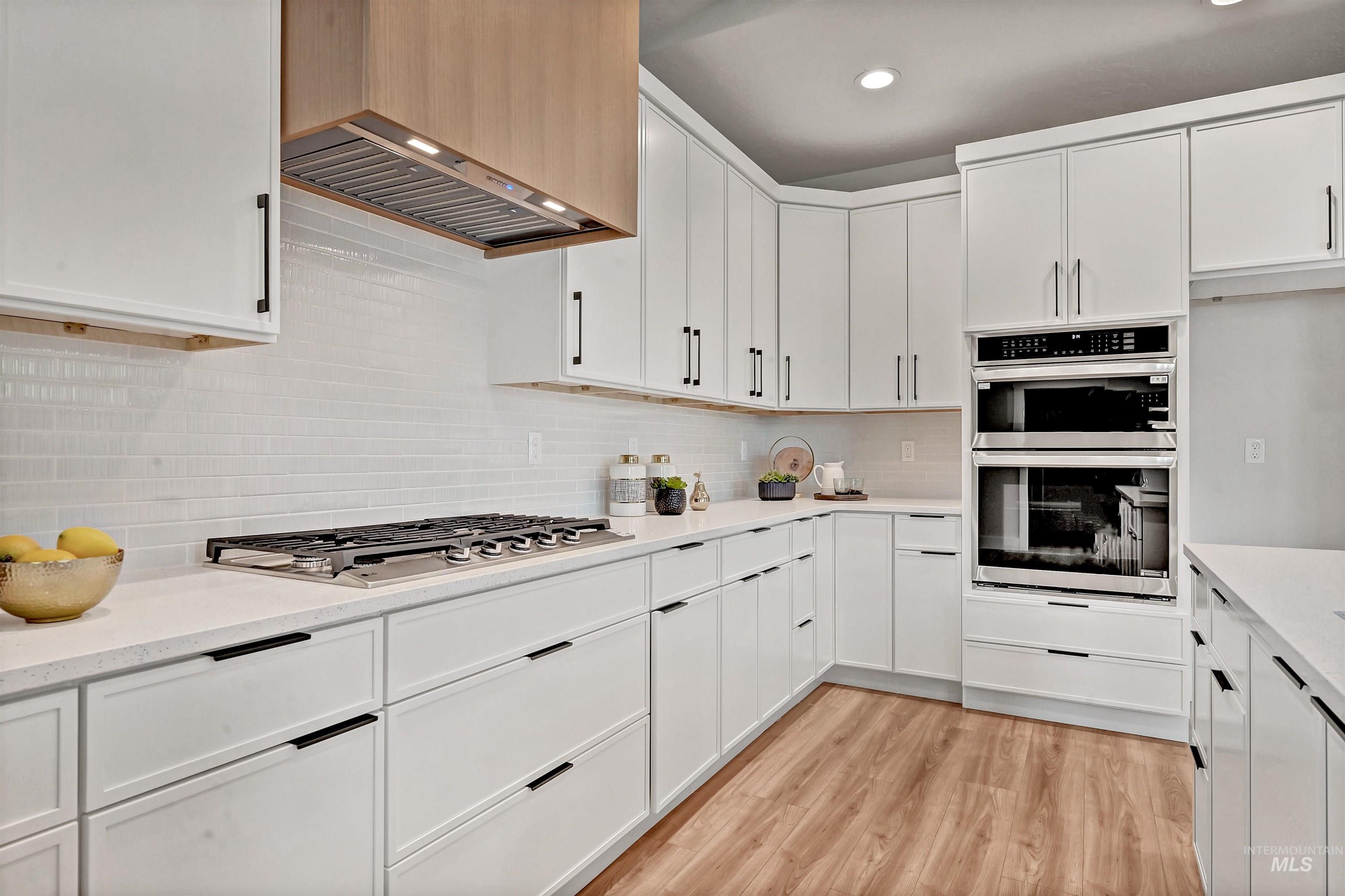 Kitchen featuring backsplash, white cabinetry, light wood-style flooring, stainless steel appliances, and recessed lighting
