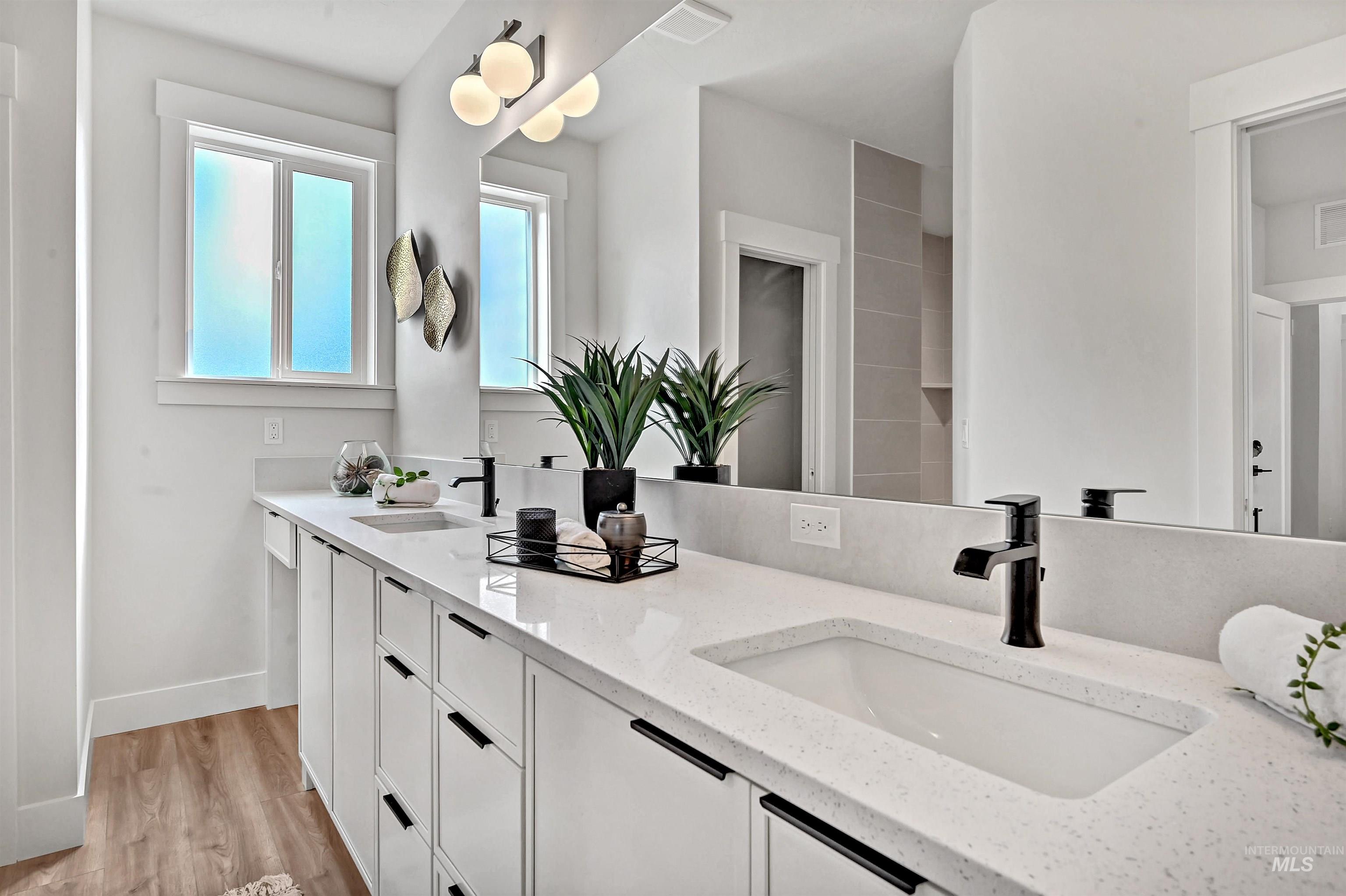 Full bath with double vanity and light wood-style flooring