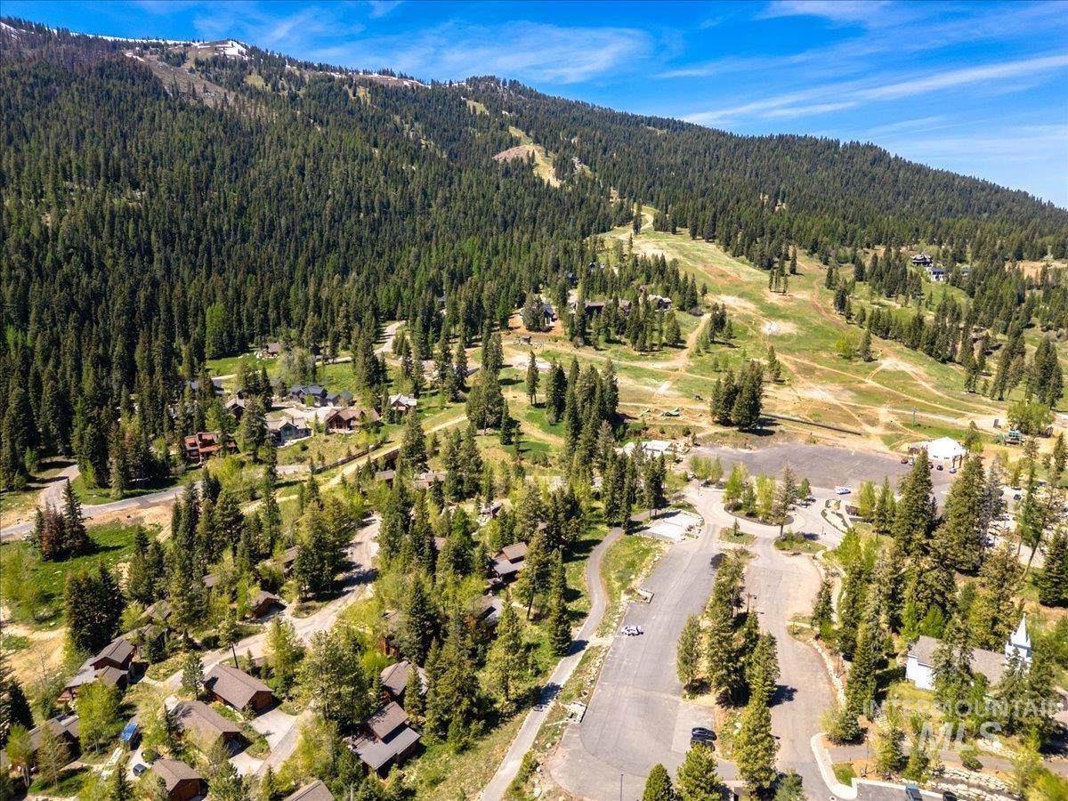 Expansive mountain landscape featuring a ski resort with multiple runs, dense evergreen forests, scattered residential properties, and paved roadways