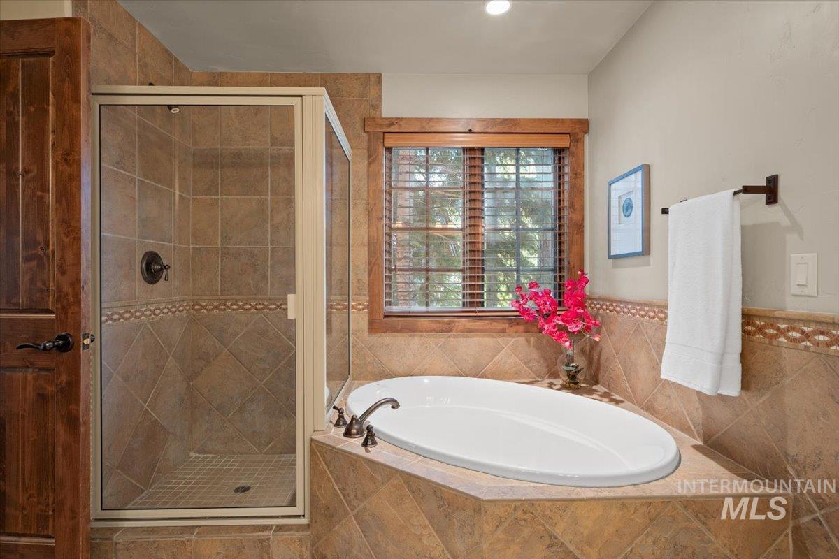 Tiled bathroom featuring a built-in soaking tub, a glass-enclosed shower with bronze fixtures, and a window with wood blinds