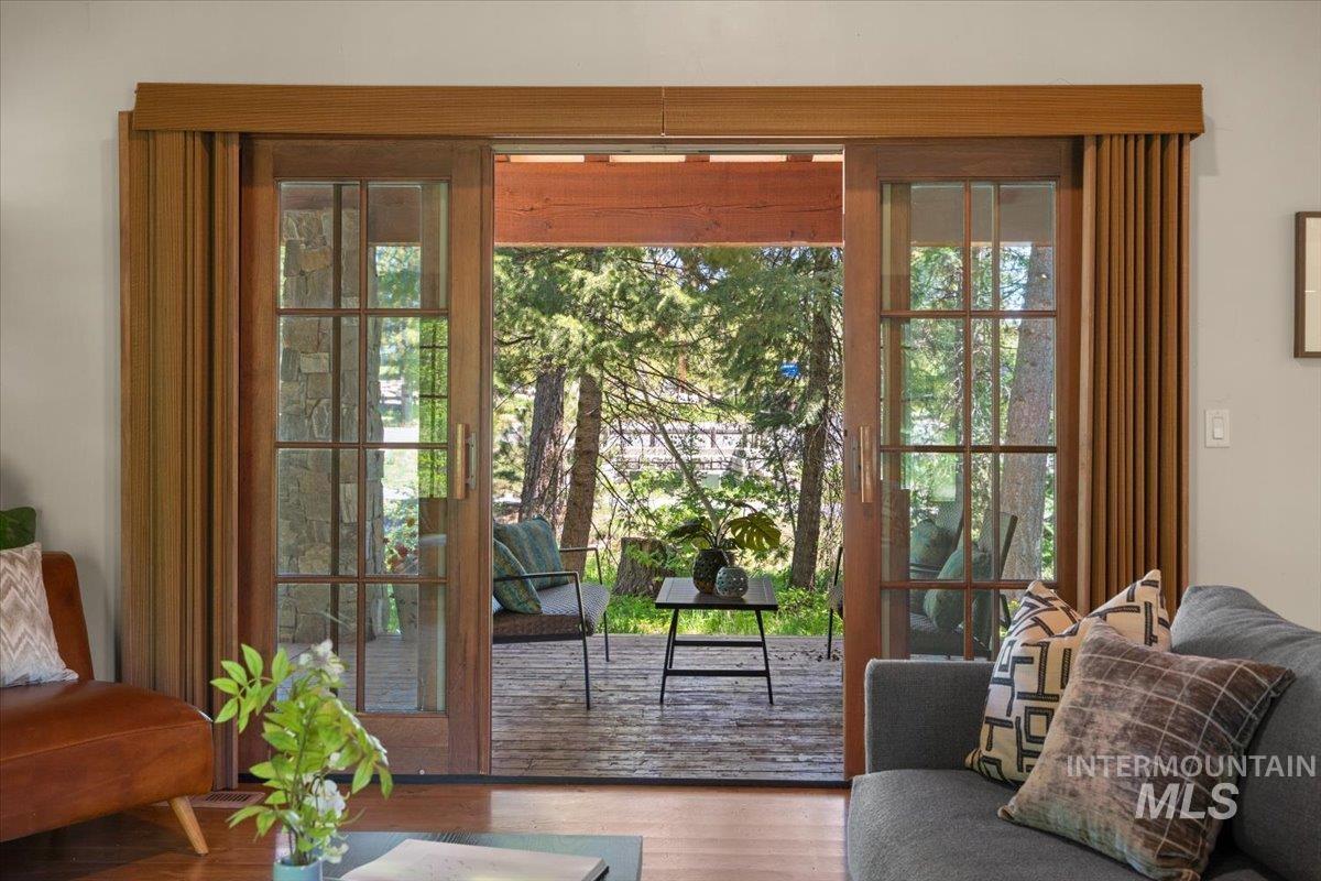 Wood-framed French doors opening onto an outdoor deck with a natural wood finish, complemented by a wood-paneled ceiling and surrounding mature trees