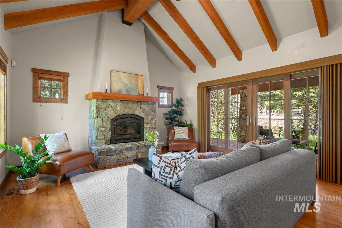 Living area featuring a stone fireplace with a wood mantel, vaulted ceilings with exposed wood beams, and wood-finish flooring